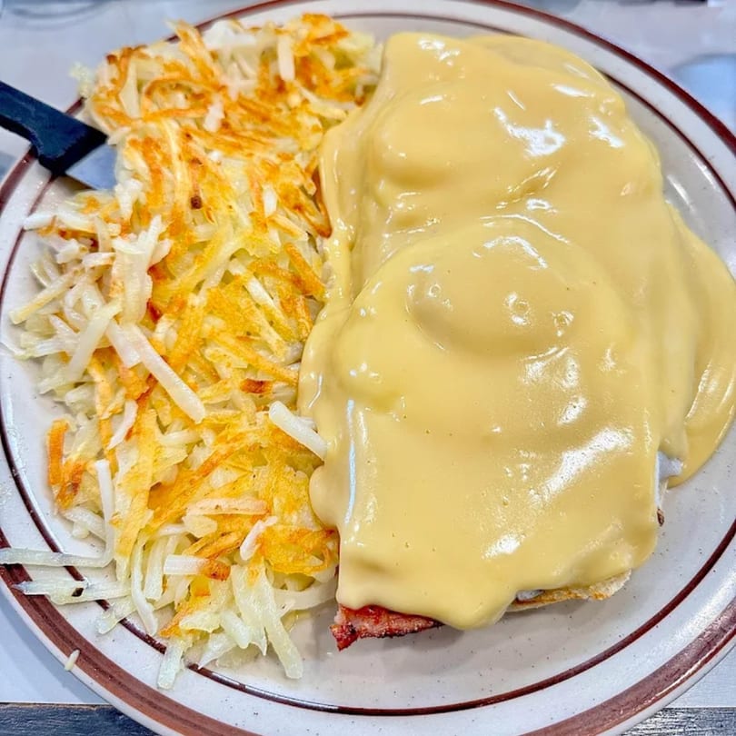 Eggs Benedict with hollandaise sauce and a side of crispy hash browns on a diner plate.